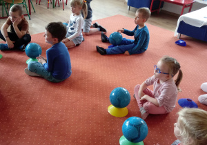 Dzieci siedzą na dywanie obok piłki